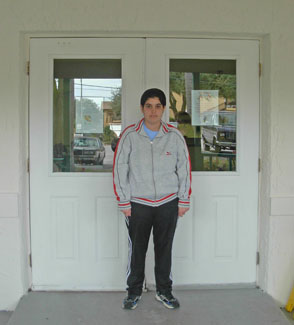 Izzy stands facing the camera in front of white double doors, with a sign just noticeable in each door’s window.